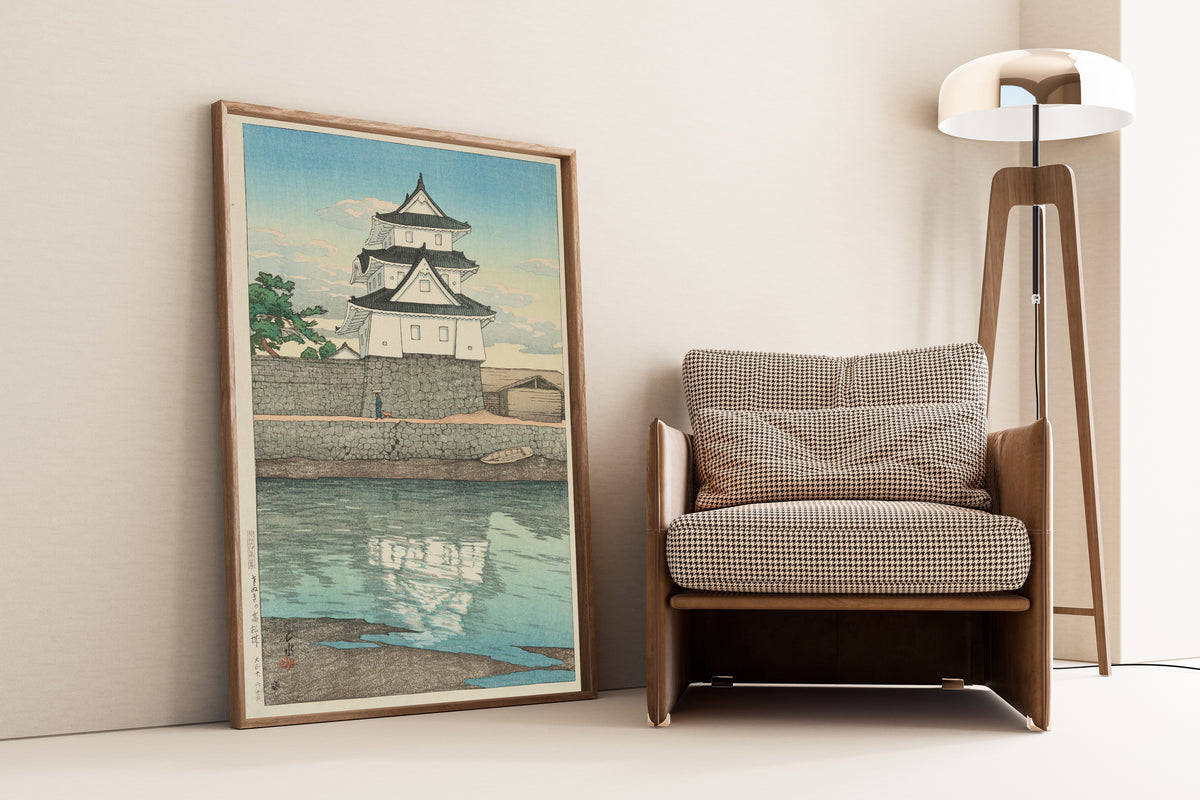Framed art print of Takamatsu Castle in Sanuki by Kawase Hasui, leaning against a wall beside an armchair and a floor lamp