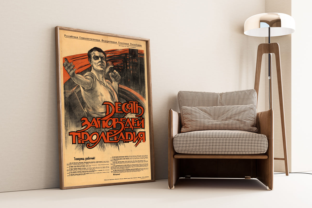 Framed art print of Ten Commandments of the Proletarian, leaning against a wall beside an armchair and a floor lamp
