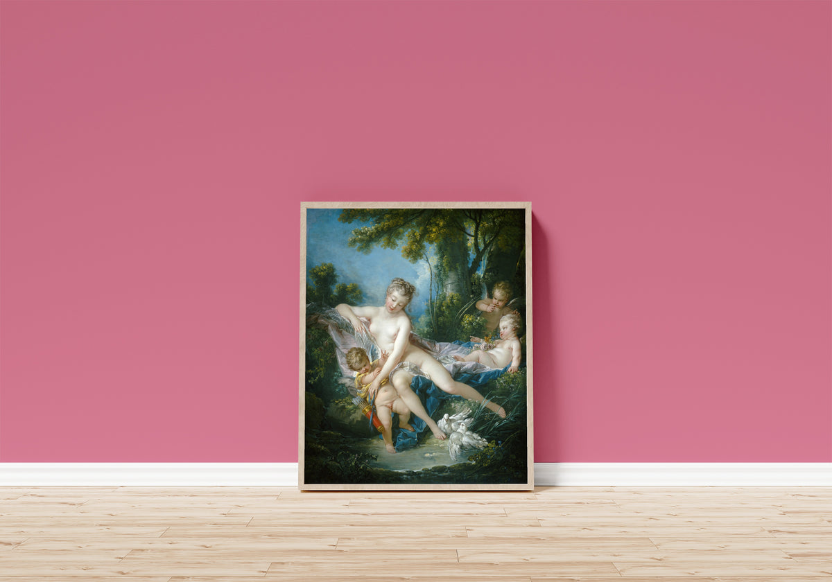 Framed art print of The Bath of Venus by François Boucher, in a light wood frame leaning on a pink wall above a wooden floor