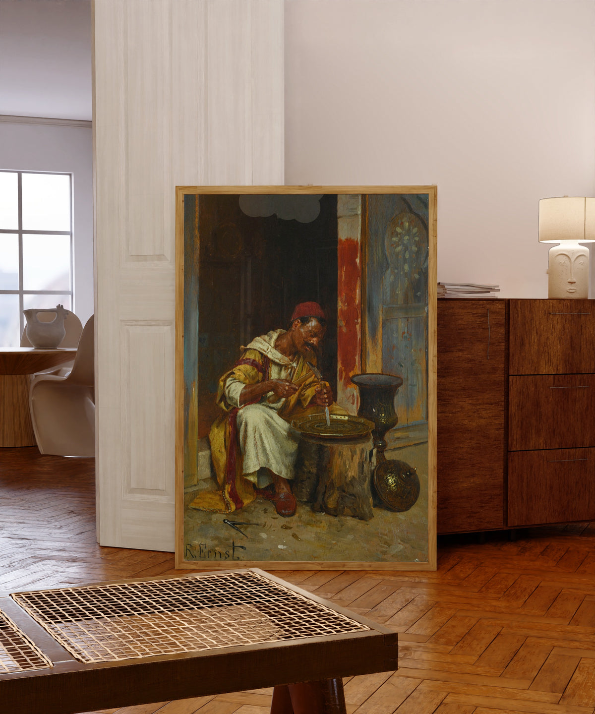 Framed art print of The Brass Worker by Rudolf Ernst, in a light wood frame leaning in a warm room with a parquet floor
