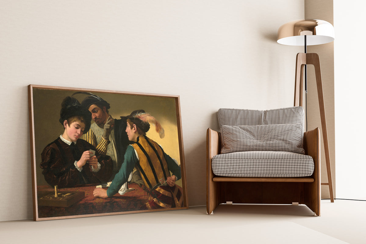 Framed art print of The Cardsharps by Caravaggio, leaning against a wall beside an armchair and a floor lamp