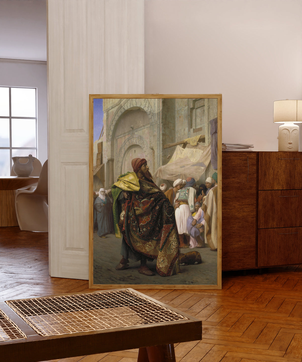 Framed art print of The Carpet Merchant of Cairo by Jean-Léon Gérôme, in a light wood frame leaning in a warm room with a parquet floor