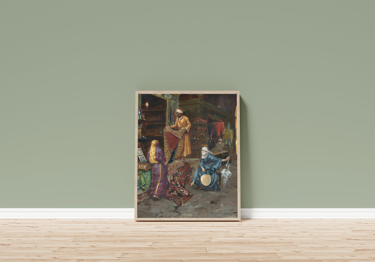 Framed art print of The Carpet Seller by Rudolf Ernst, in a light wood frame leaning on a sage green wall above a wooden floor
