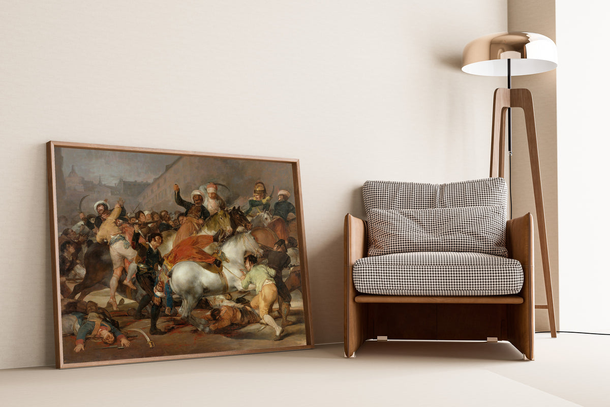 Framed art print of The Charge of the Mamelukes by Francisco de Goya, leaning against a wall beside an armchair and a floor lamp