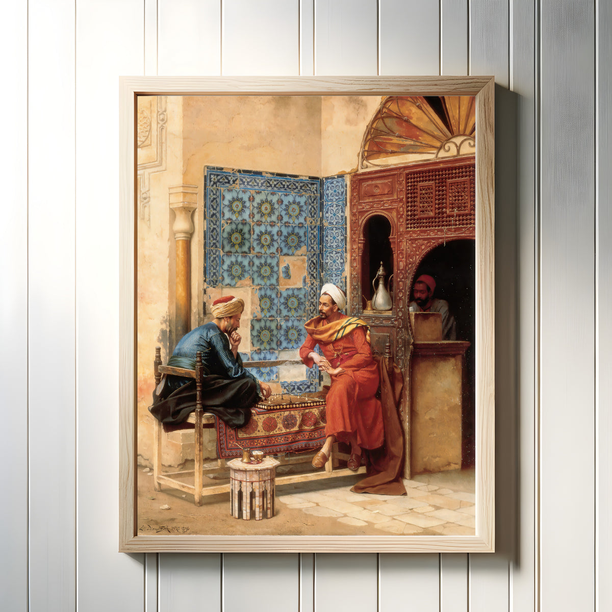Framed art print of The Chess Game by Ludwig Deutsch, in a light wood frame on a white panelled wall