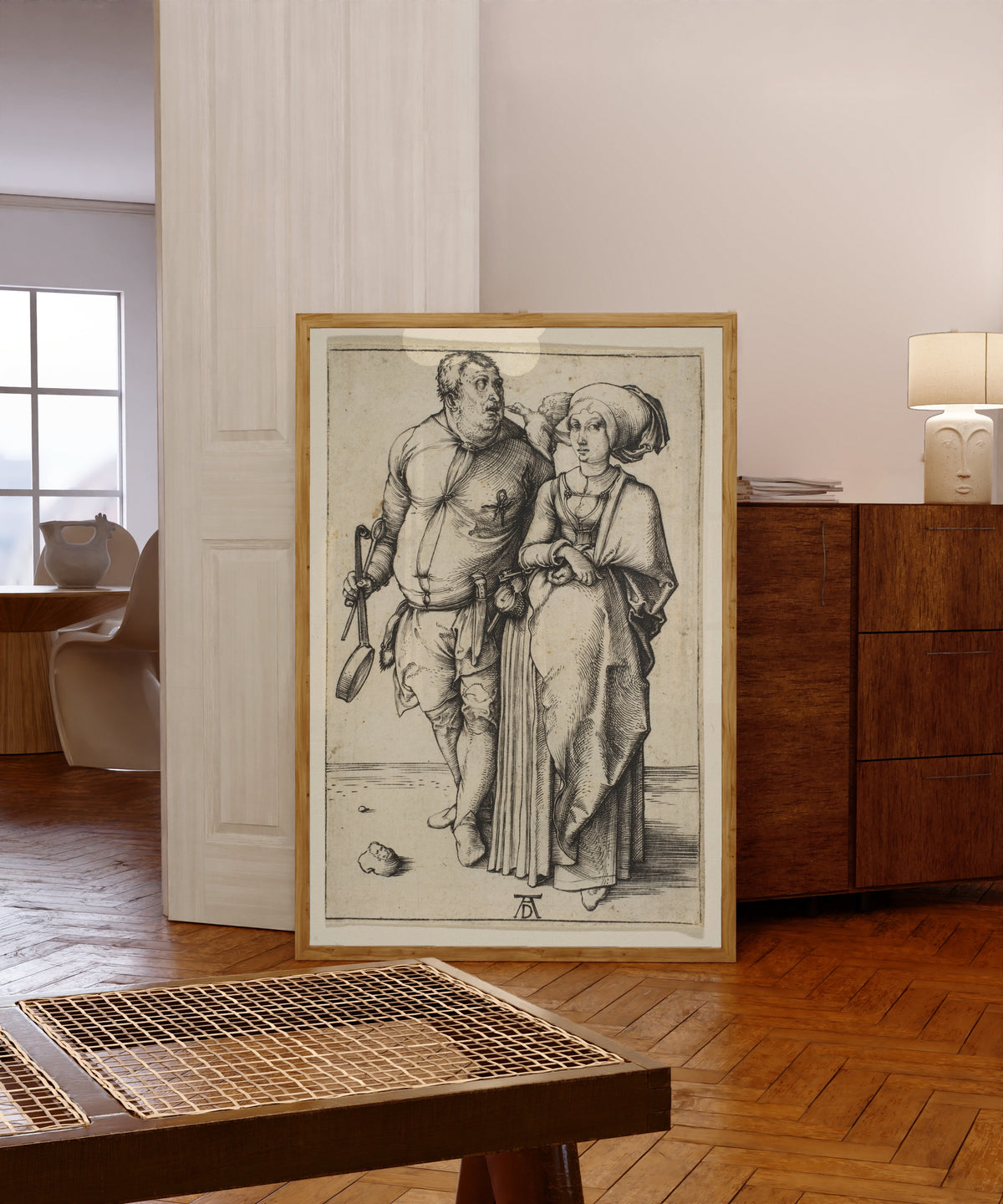 Framed art print of The Cook and His Wife by Albrecht Dürer, in a light wood frame leaning in a warm room with a parquet floor