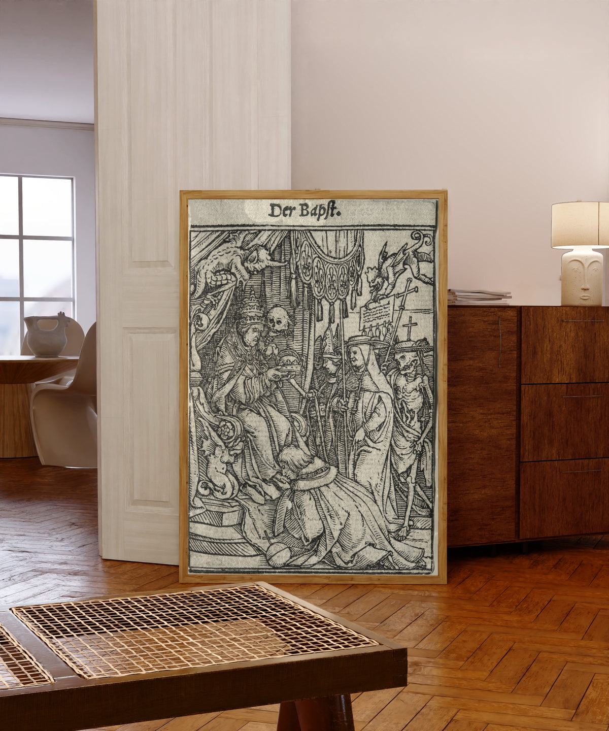 Framed art print of The Dance of Death: Der Bapst (The Pope) by Hans Holbein the Younger, in a light wood frame leaning in a warm room with a parquet floor