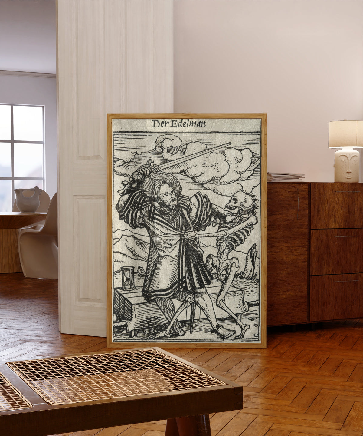 Framed art print of The Dance of Death: Der Edelman (The… by Hans Holbein the Younger, in a light wood frame leaning in a warm room with a parquet floor