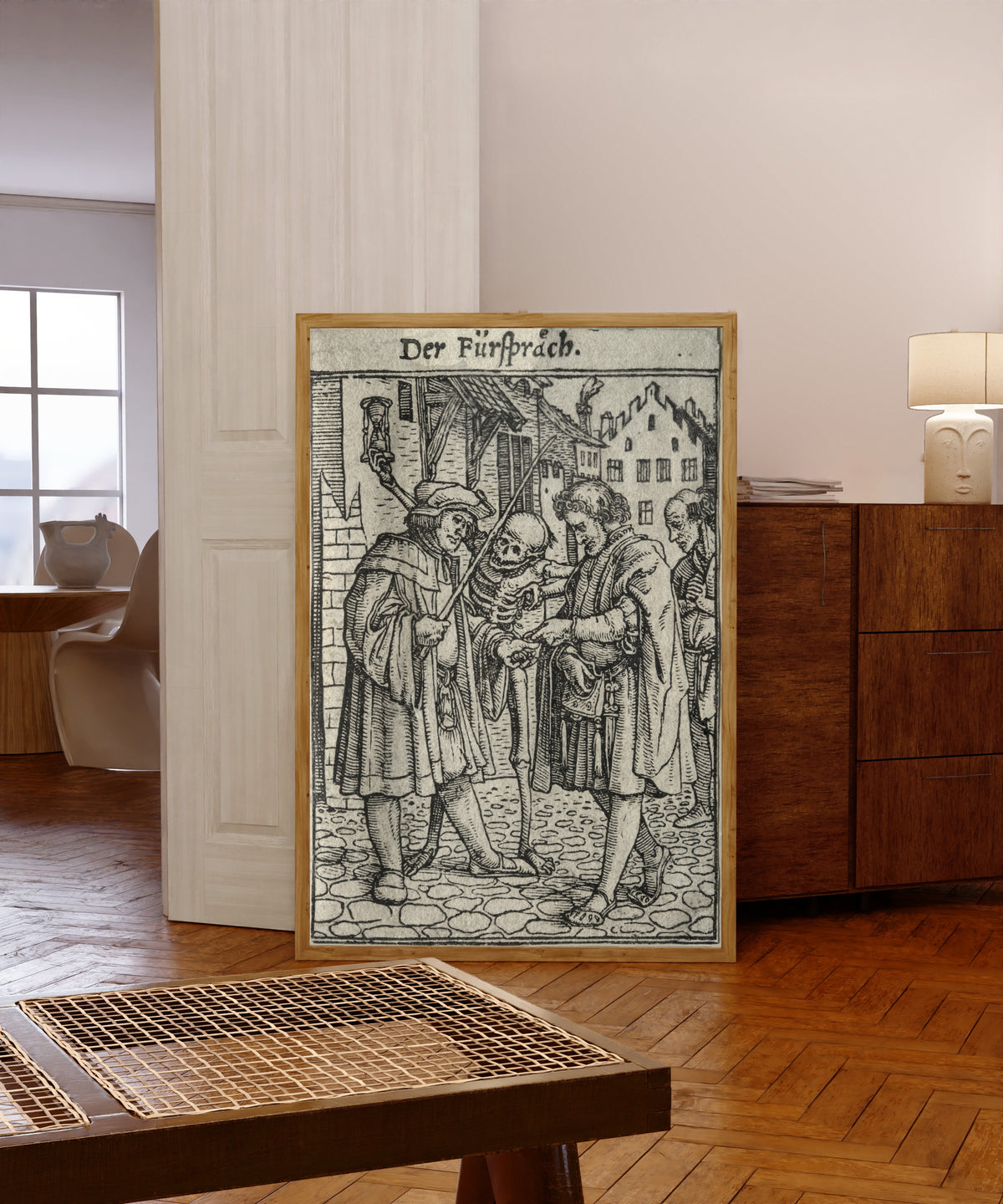 Framed art print of The Dance of Death: Der Fürspräch (The… by Hans Holbein the Younger, in a light wood frame leaning in a warm room with a parquet floor