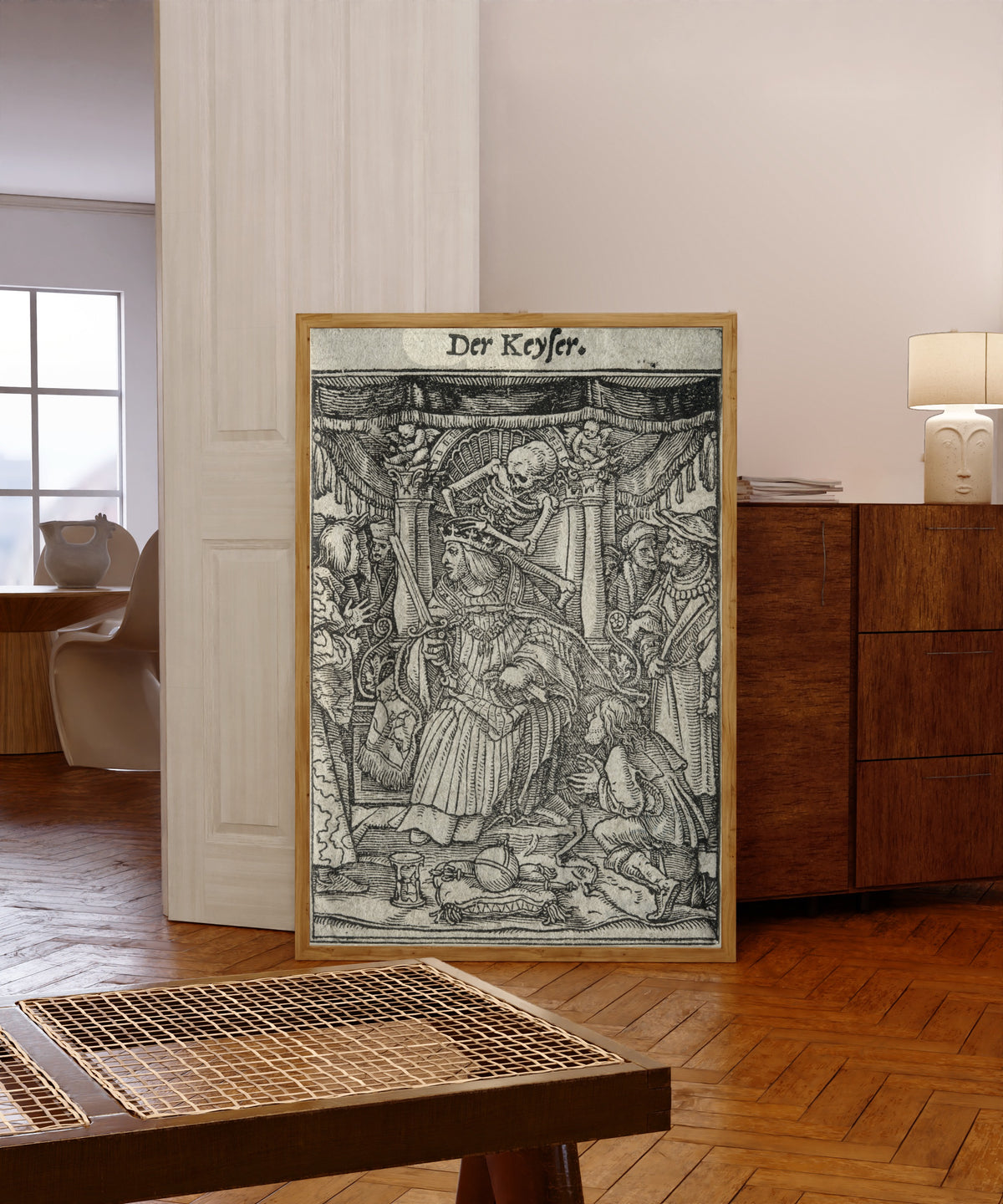 Framed art print of The Dance of Death: Der Keyser (The Emperor) by Hans Holbein the Younger, in a light wood frame leaning in a warm room with a parquet floor