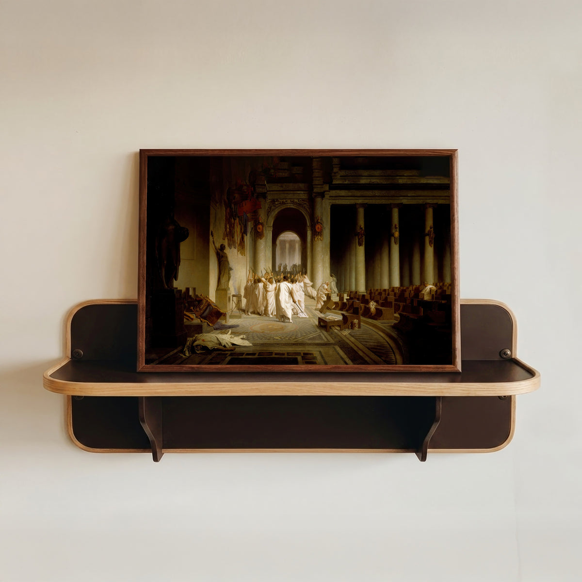 Framed art print of The Death of Caesar by Jean-Léon Gérôme, in a dark wood frame resting on a wall shelf