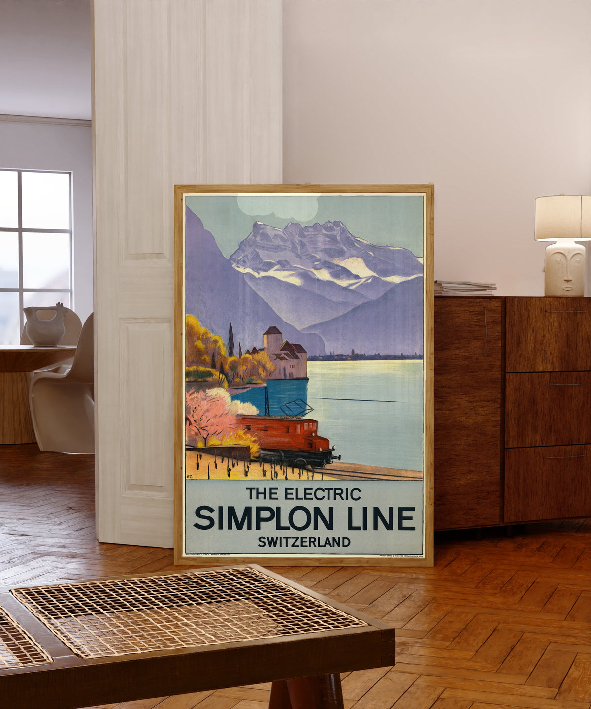 Framed art print of The Electric Simplon Line: Switzerland by Emil Cardinaux, in a light wood frame leaning in a warm room with a parquet floor