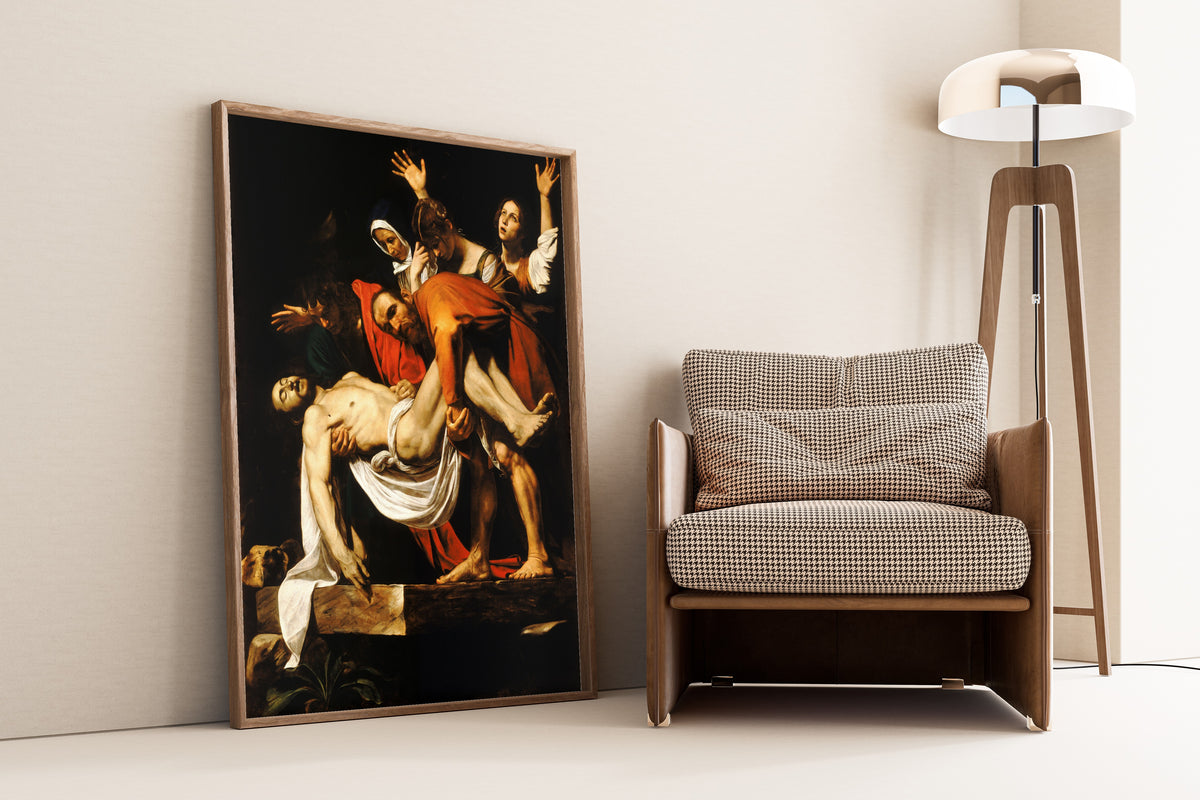 Framed art print of The Entombment of Christ by Caravaggio, leaning against a wall beside an armchair and a floor lamp