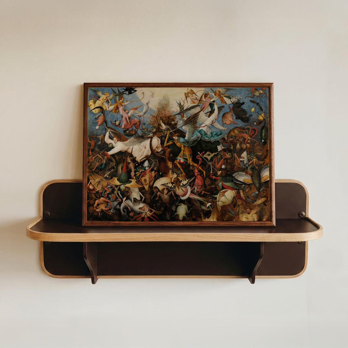 Framed art print of The Fall of the Rebel Angels by Pieter Bruegel the Elder, in a dark wood frame resting on a wall shelf
