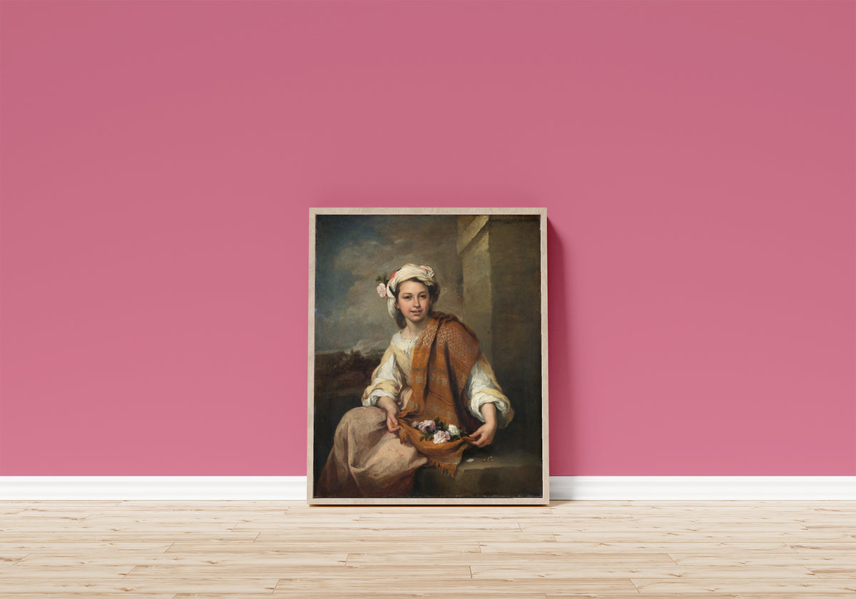 Framed art print of The Flower Girl by Bartolomé Esteban Murillo, in a light wood frame leaning on a pink wall above a wooden floor
