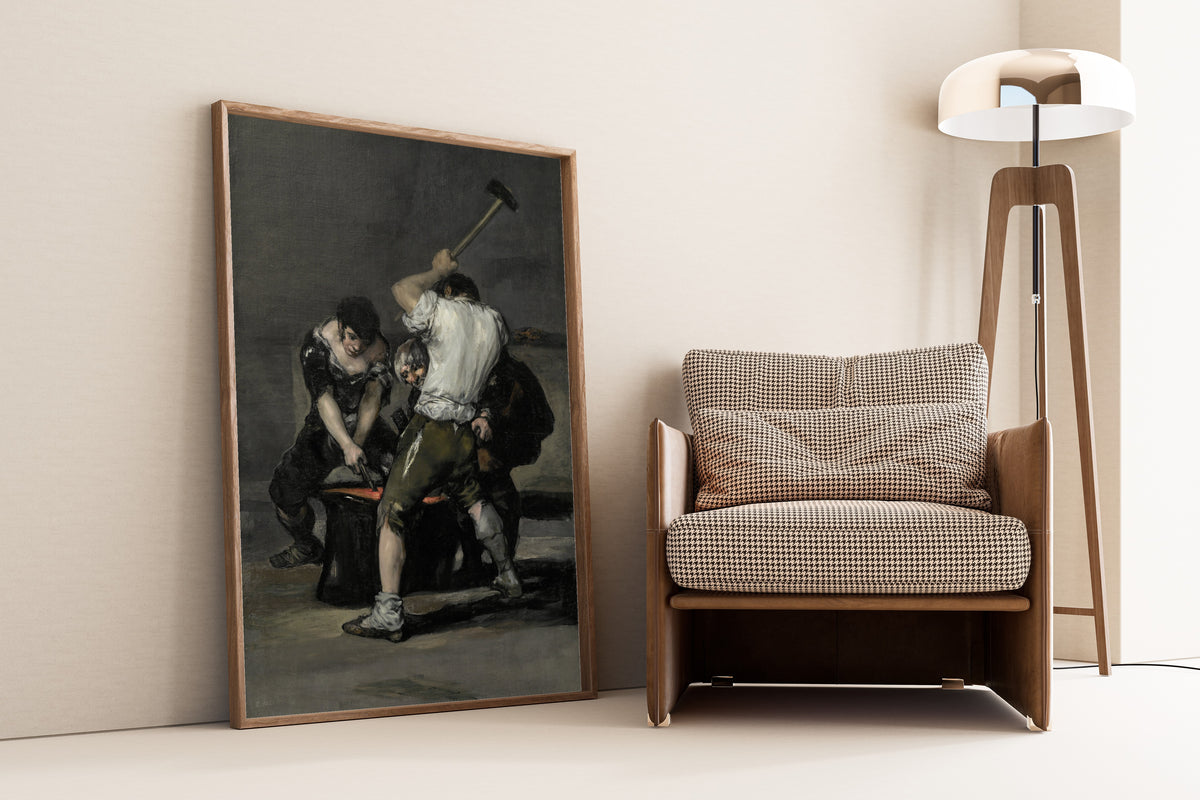 Framed art print of The Forge by Francisco de Goya, leaning against a wall beside an armchair and a floor lamp