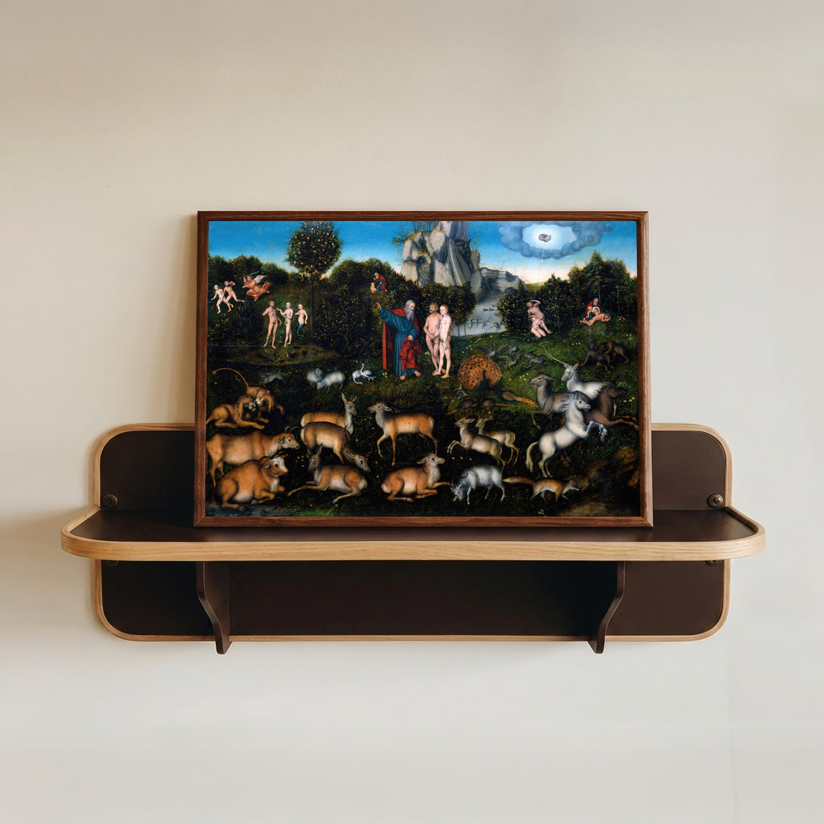 Framed art print of The Garden of Eden by Lucas Cranach the Elder, in a dark wood frame resting on a wall shelf