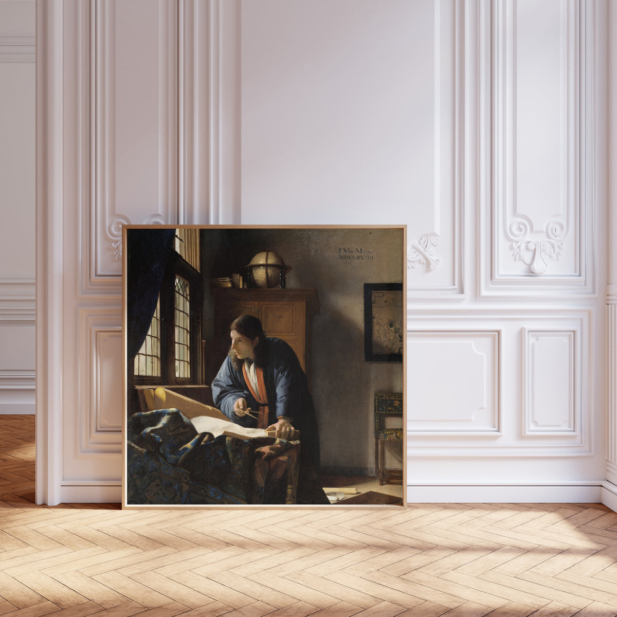 Framed art print of The Geographer by Johannes Vermeer, leaning against pale pink panelling on a herringbone floor