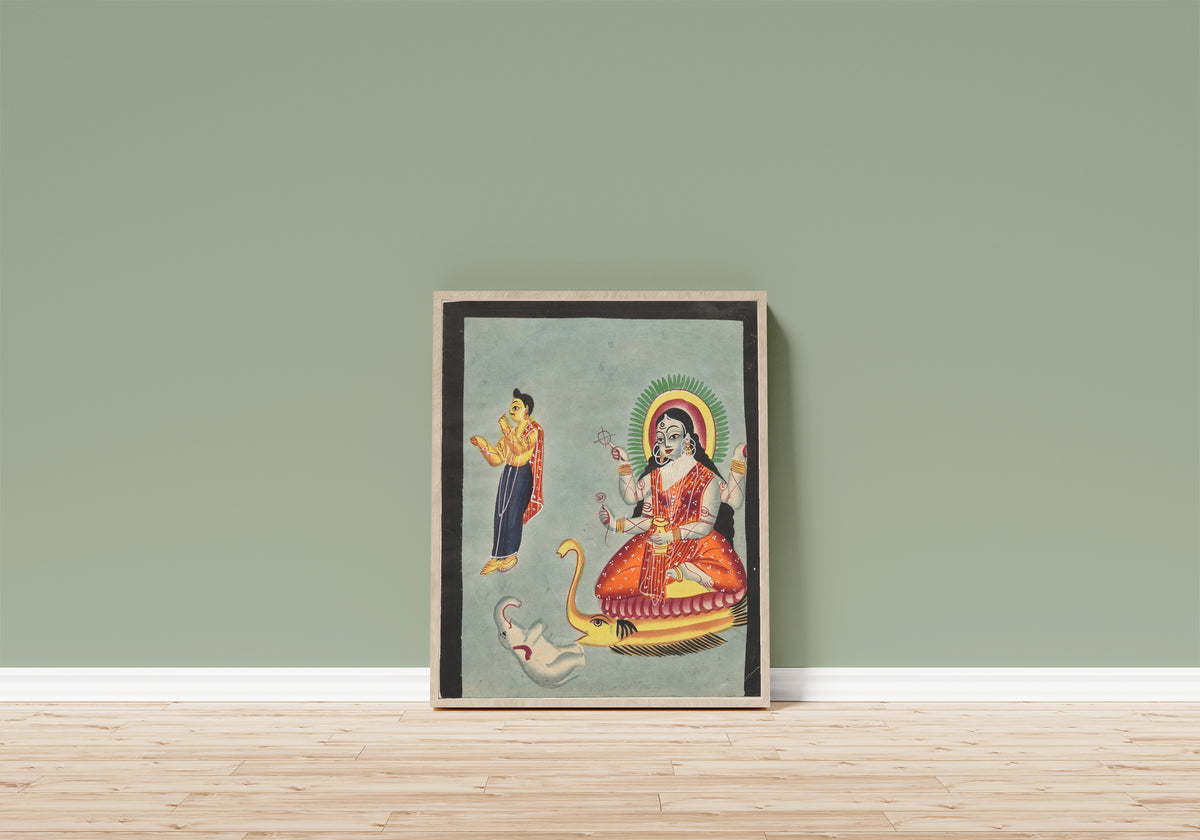 Framed art print of The Goddess Ganga, from a Kalighat album by Kalighat painter, in a light wood frame leaning on a sage green wall above a wooden floor