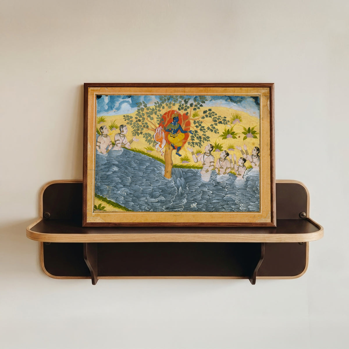 Framed art print of The Gopis Plead with Krishna to Return Their Clothing by Bikaner school, in a dark wood frame resting on a wall shelf