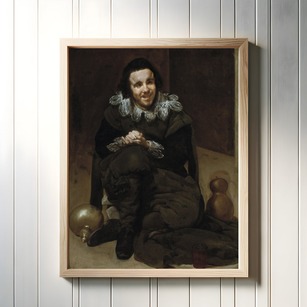 Framed art print of The Jester Calabacillas by Diego Velázquez, in a light wood frame on a white panelled wall
