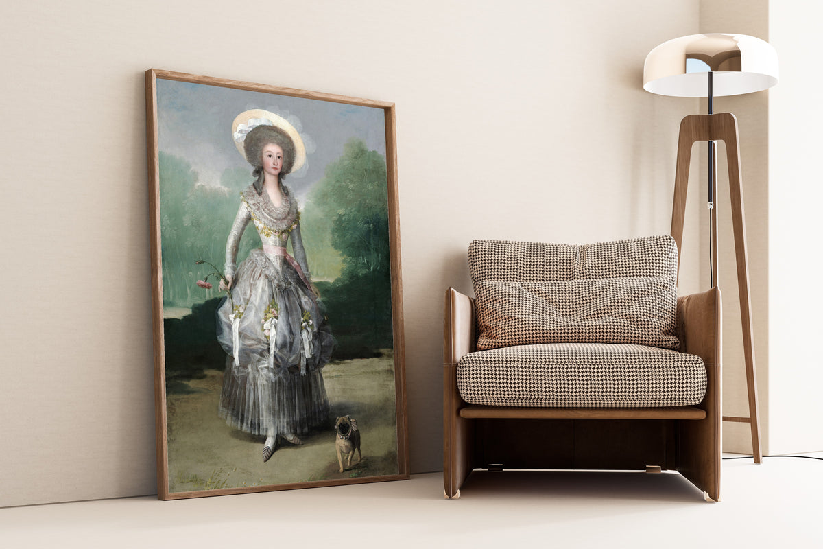 Framed art print of The Marquesa de Pontejos by Francisco de Goya, leaning against a wall beside an armchair and a floor lamp