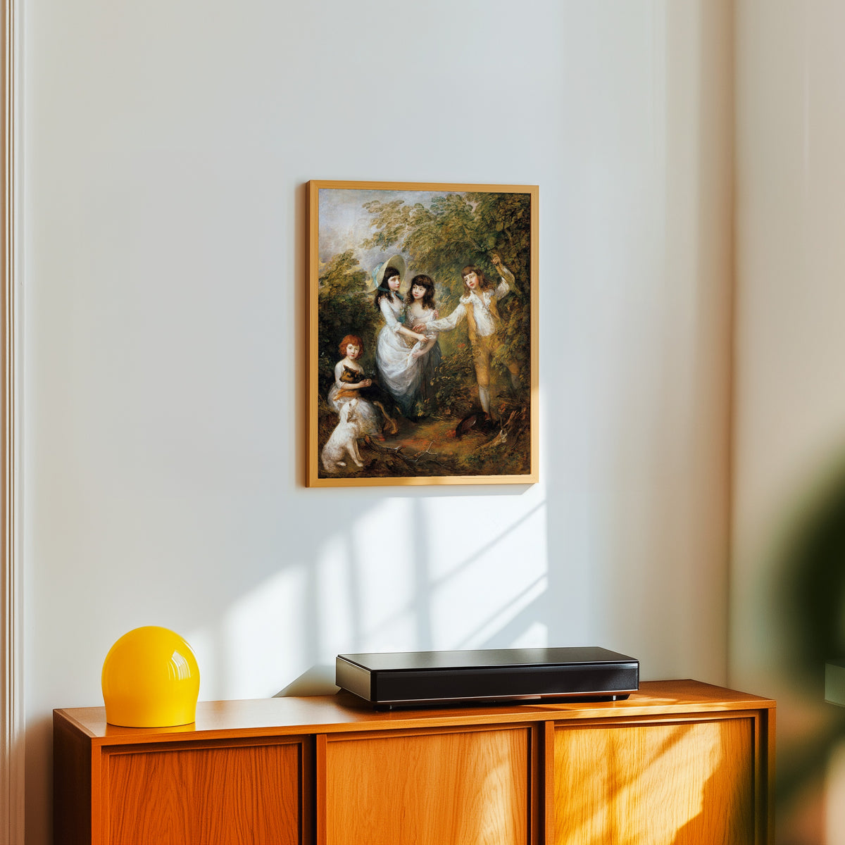 Framed art print of The Marsham Children by Thomas Gainsborough, in a light wood frame on a white wall above an orange sideboard
