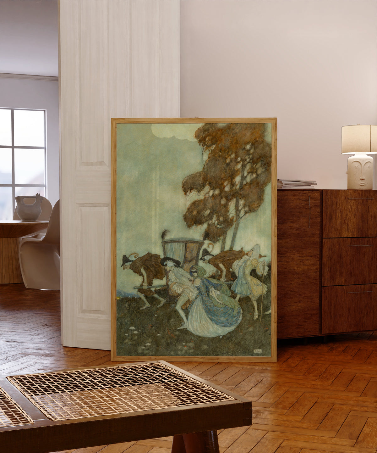 Framed art print of The Masqueraders by Edmund Dulac, in a light wood frame leaning in a warm room with a parquet floor