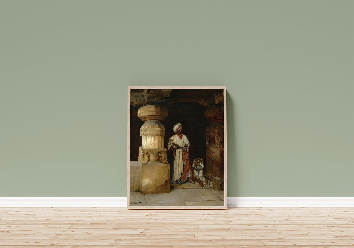 Framed art print of The Palace Guard (with tiger) by Rudolf Ernst, in a light wood frame leaning on a sage green wall above a wooden floor