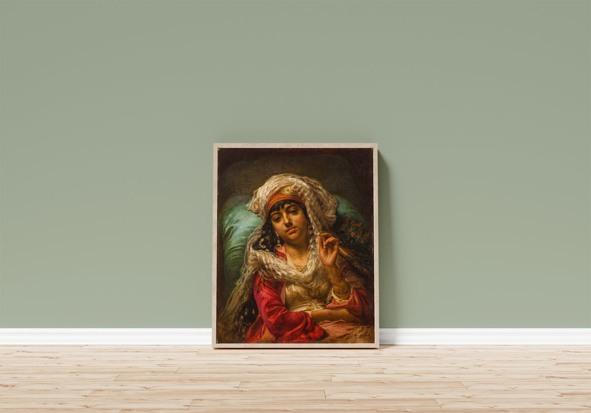 Framed art print of The Peacock Fan by Frederick Arthur Bridgman, in a light wood frame leaning on a sage green wall above a wooden floor