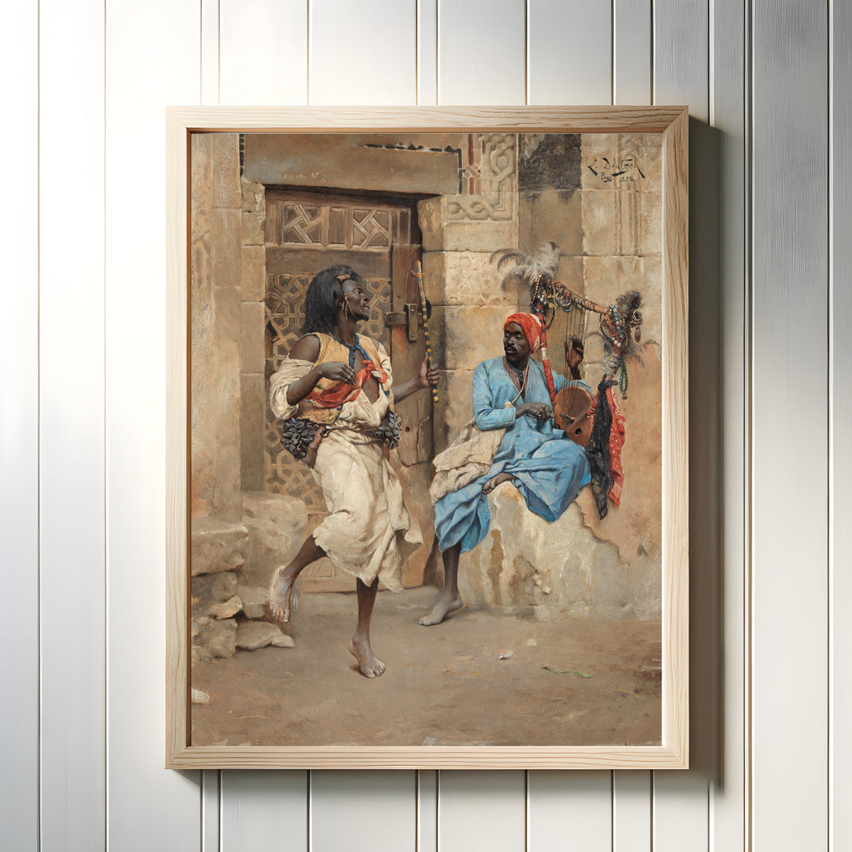 Framed art print of The Performance by Ludwig Deutsch, in a light wood frame on a white panelled wall