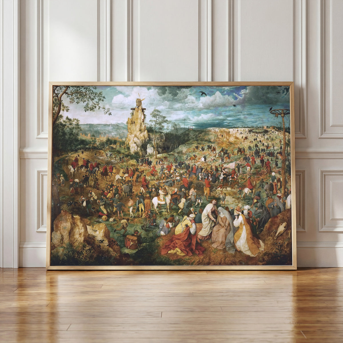 Framed art print of The Procession to Calvary by Pieter Bruegel the Elder, in a light wood frame leaning against a panelled white wall