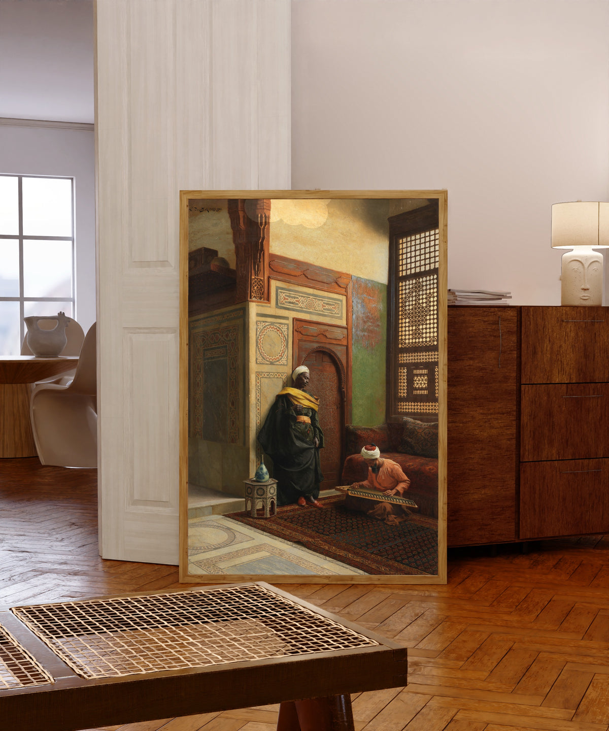 Framed art print of The Qanun Player by Ludwig Deutsch, in a light wood frame leaning in a warm room with a parquet floor