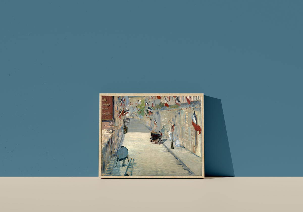 Framed art print of The Rue Mosnier with Flags by Édouard Manet, in a light wood frame leaning on a blue wall