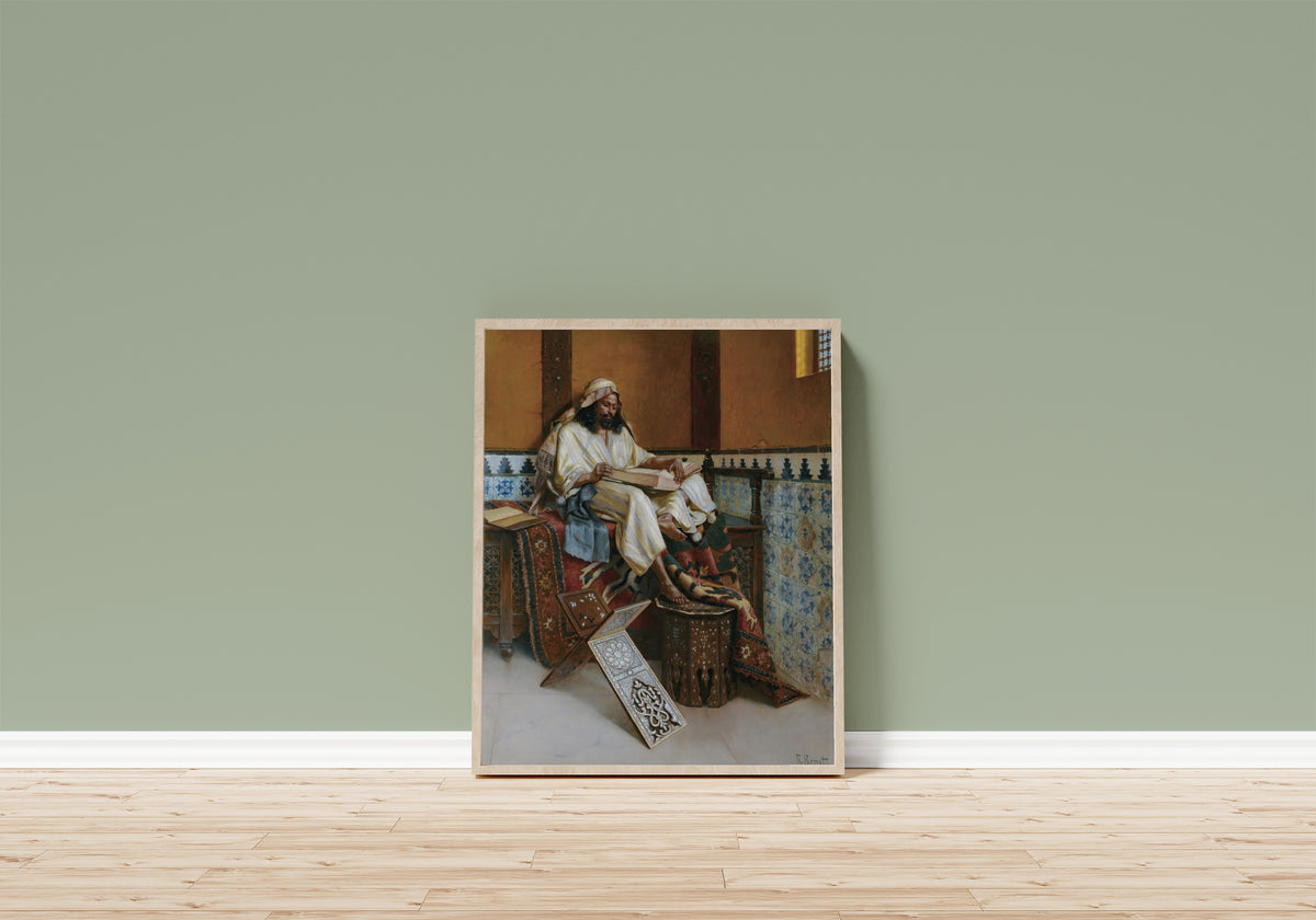 Framed art print of The Scholar by Rudolf Ernst, in a light wood frame leaning on a sage green wall above a wooden floor