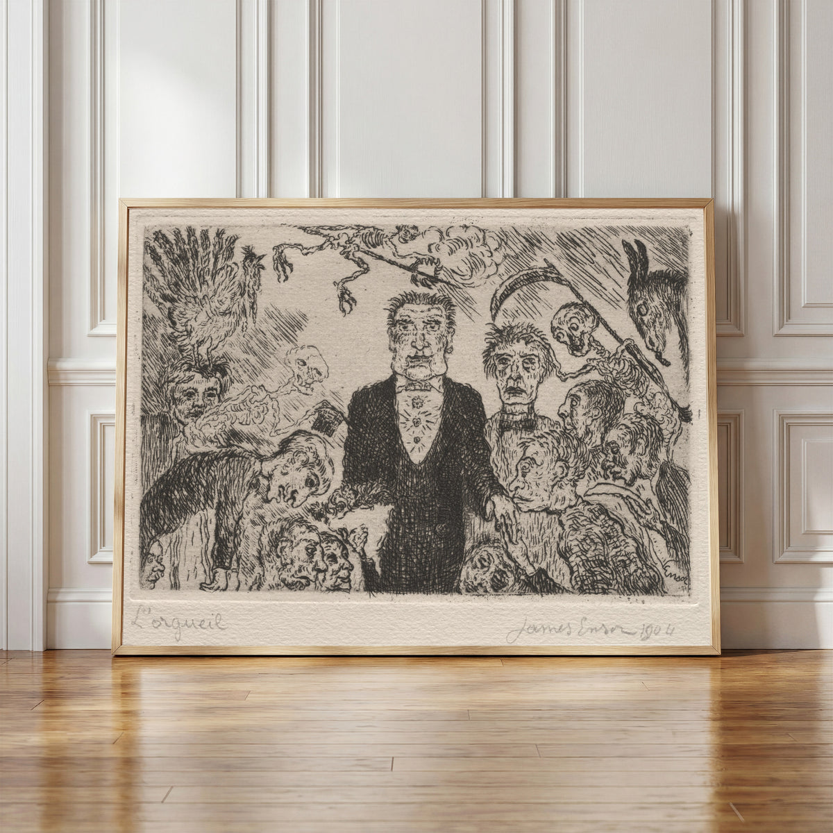 Framed art print of The Seven Deadly Sins: Pride by James Ensor, in a light wood frame leaning against a panelled white wall