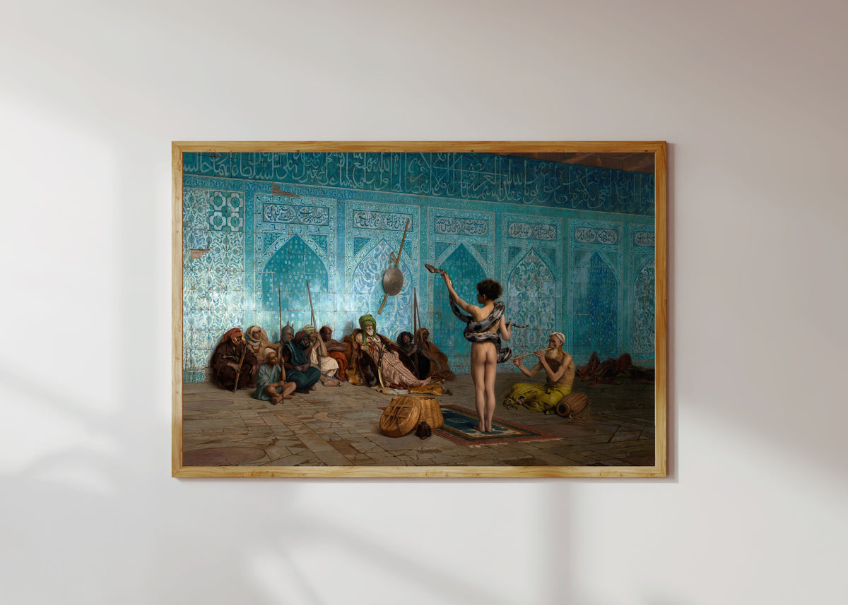 Framed art print of The Snake Charmer by Jean-Léon Gérôme, in a light wood frame on a sunlit white wall