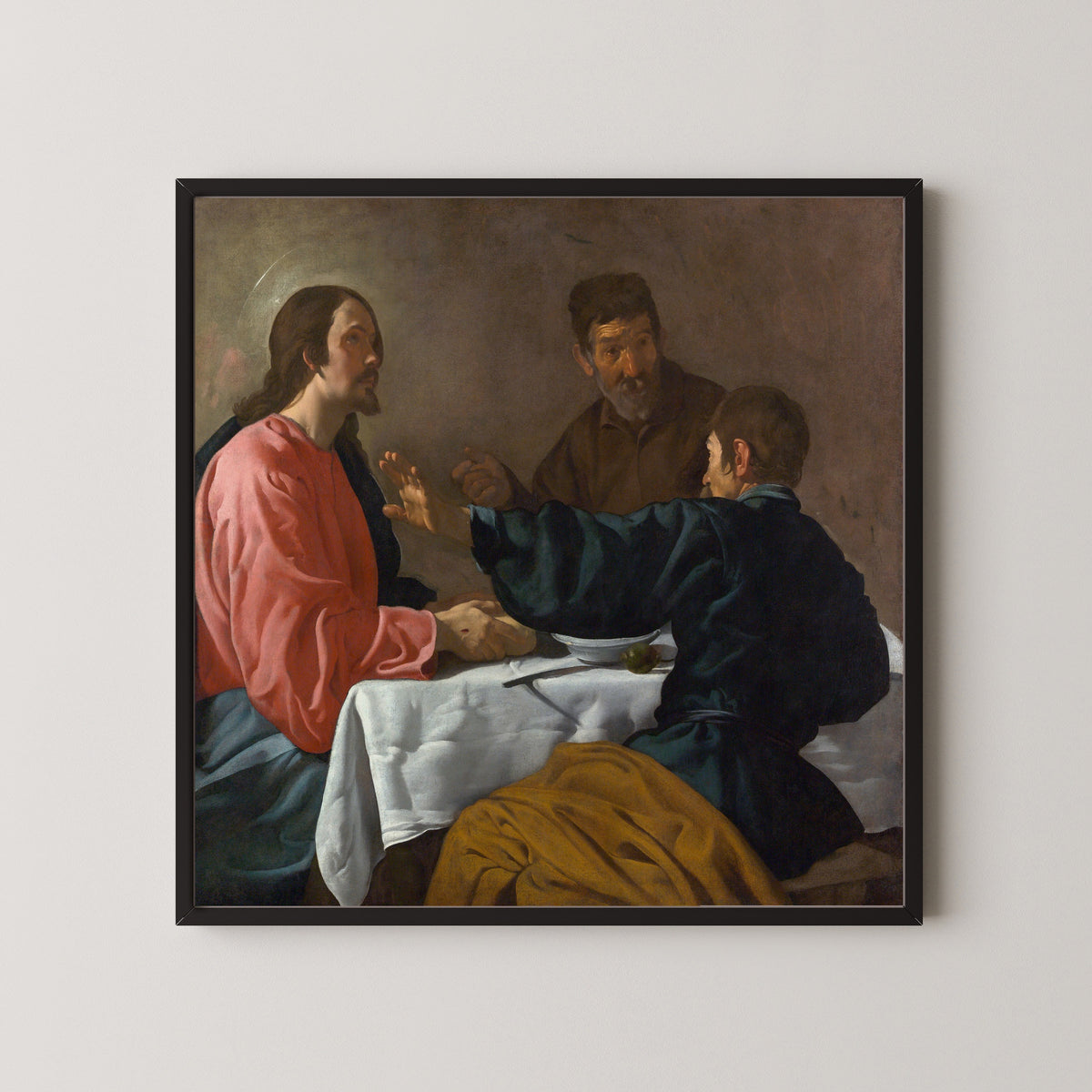 Framed art print of The Supper at Emmaus by Diego Velázquez, in a black frame on a pale wall