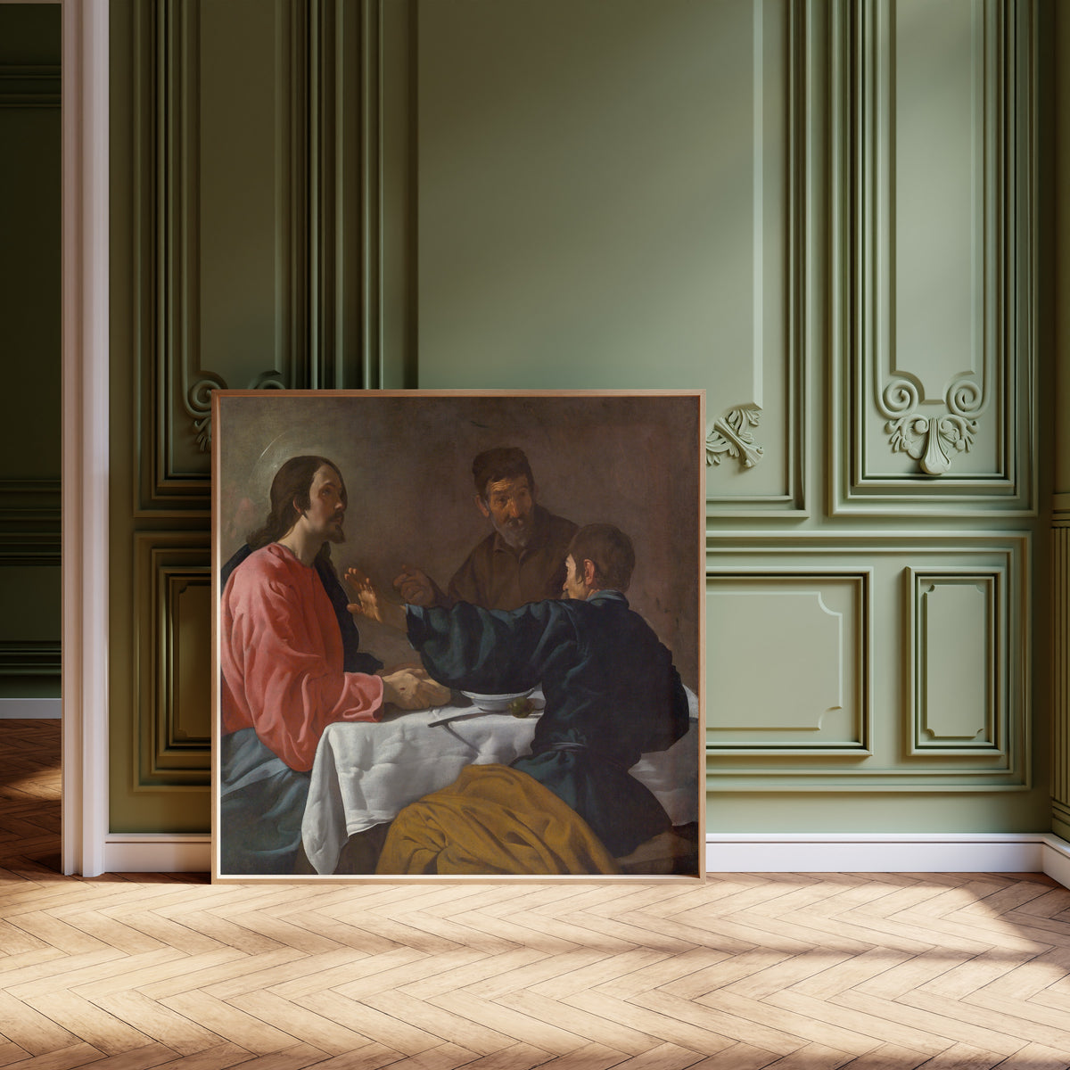 Framed art print of The Supper at Emmaus by Diego Velázquez, leaning against olive-green panelling on a herringbone floor