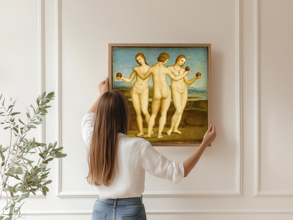 Framed art print of The Three Graces by Raphael, hung on a panelled wall