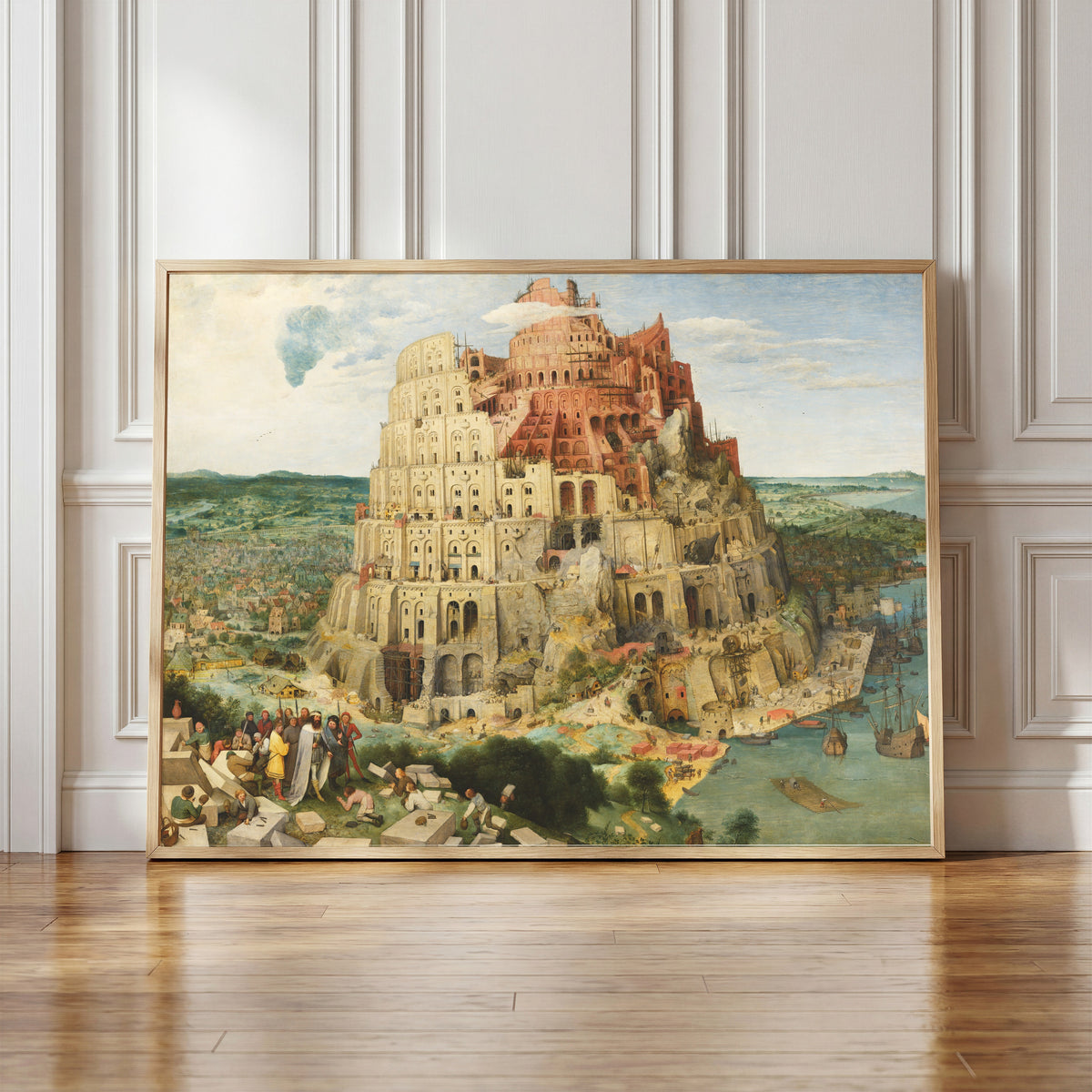 Framed art print of The Tower of Babel (Vienna) by Pieter Bruegel the Elder, in a light wood frame leaning against a panelled white wall