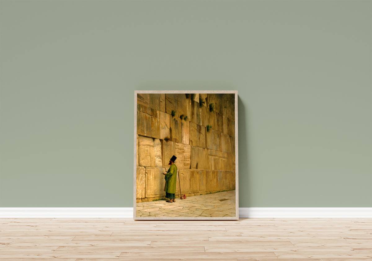 Framed art print of The Wailing Wall by Jean-Léon Gérôme, in a light wood frame leaning on a sage green wall above a wooden floor