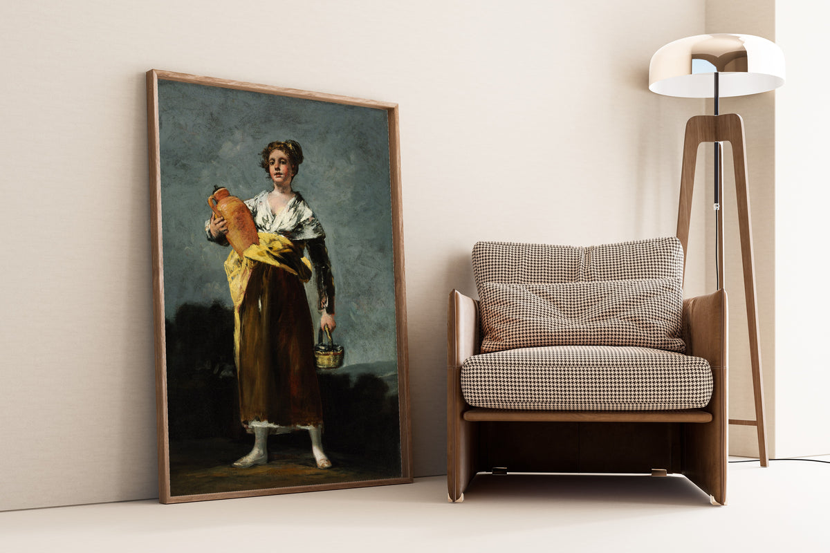 Framed art print of The Water Carrier (La Aguadora) by Francisco de Goya, leaning against a wall beside an armchair and a floor lamp
