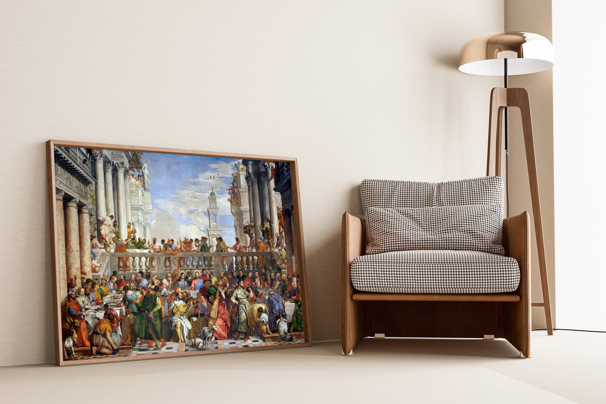 Framed art print of The Wedding at Cana by Paolo Veronese, leaning against a wall beside an armchair and a floor lamp
