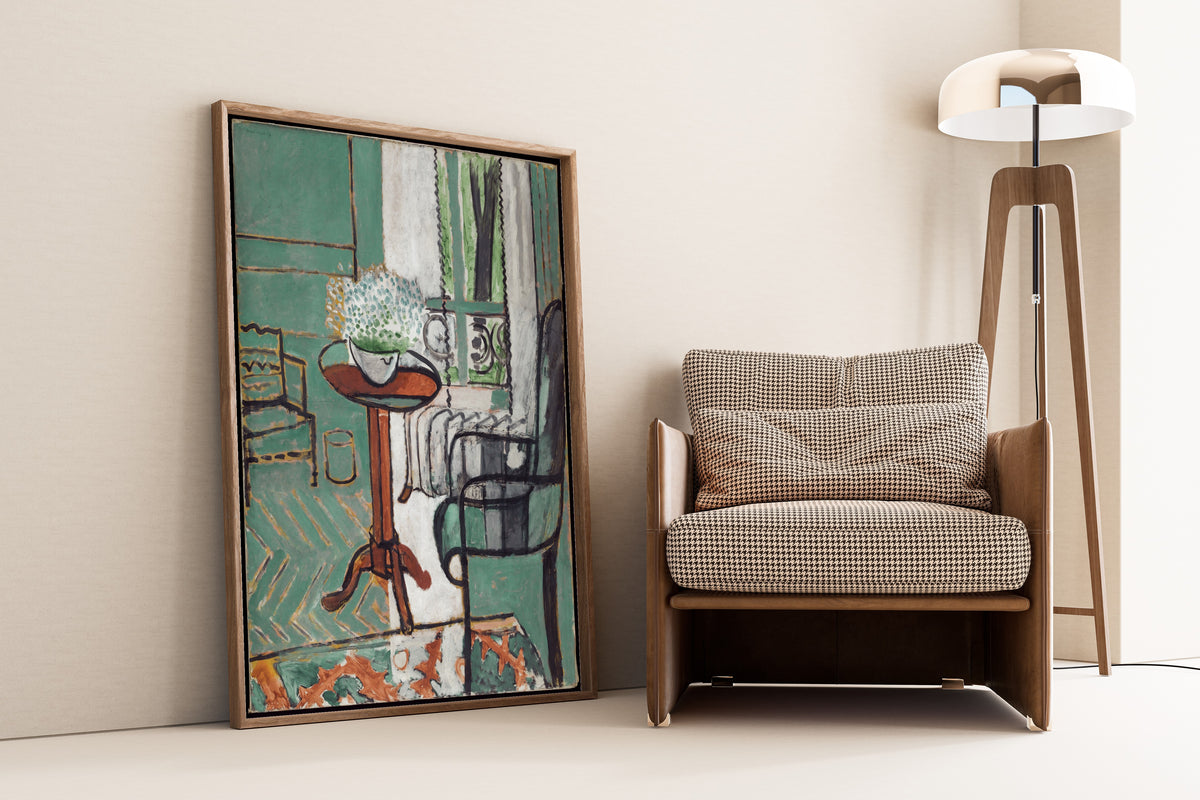 Framed art print of The Window by Henri Matisse, leaning against a wall beside an armchair and a floor lamp