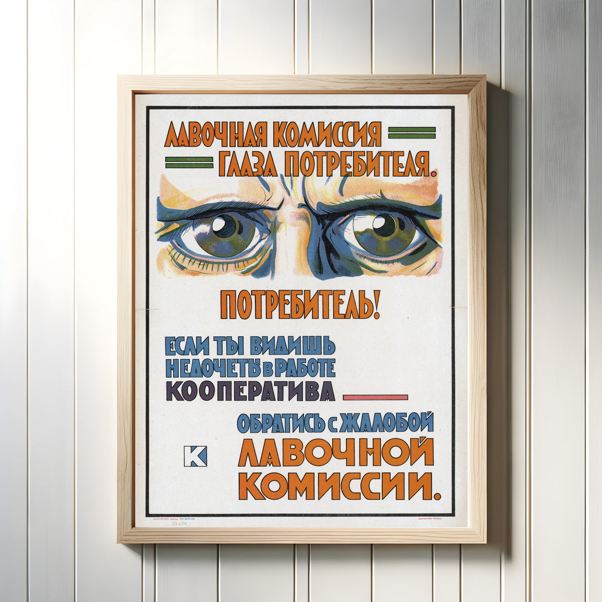 Framed art print of The shop commission: the eyes of the consumer, in a light wood frame on a white panelled wall