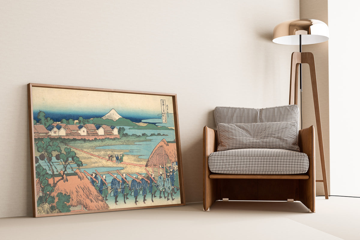 Framed art print of Thirty-six Views of Mount Fuji: Fuji Seen in the… by Katsushika Hokusai, leaning against a wall beside an armchair and a floor lamp