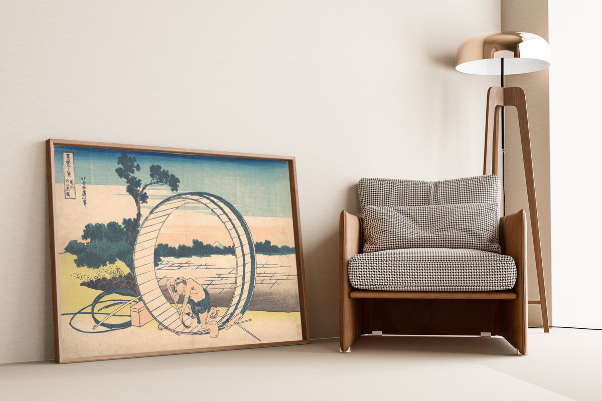 Framed art print of Thirty-six Views of Mount Fuji: Fujimigahara in Owari… by Katsushika Hokusai, leaning against a wall beside an armchair and a floor lamp