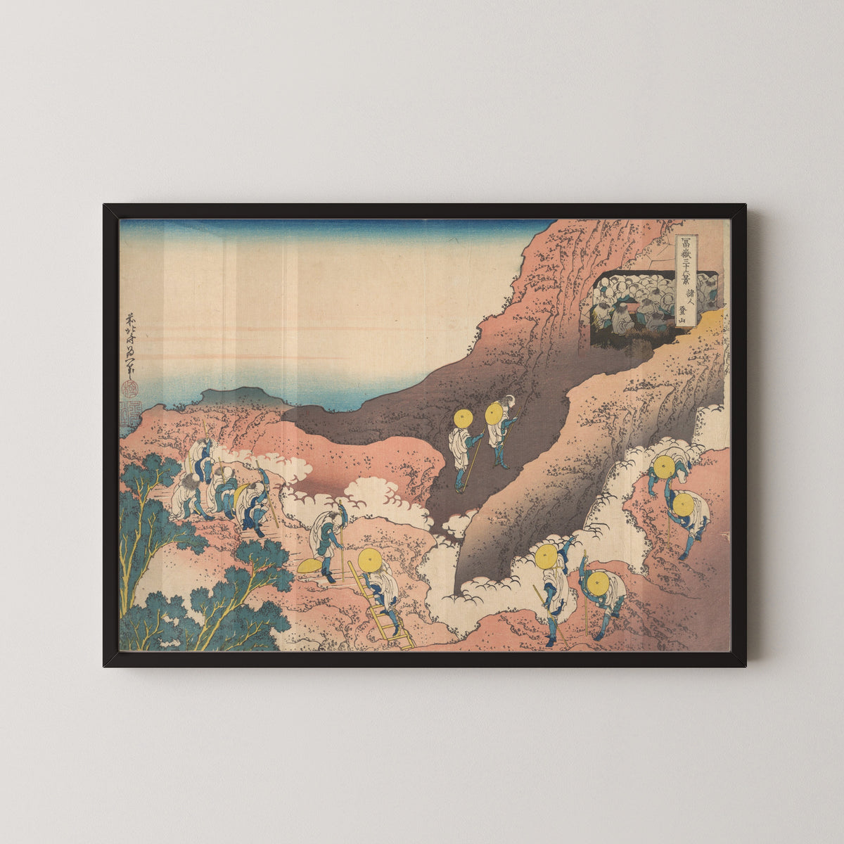 Framed art print of Thirty-six Views of Mount Fuji: Groups of Mountain Climbers by Katsushika Hokusai, in a black frame on a pale wall