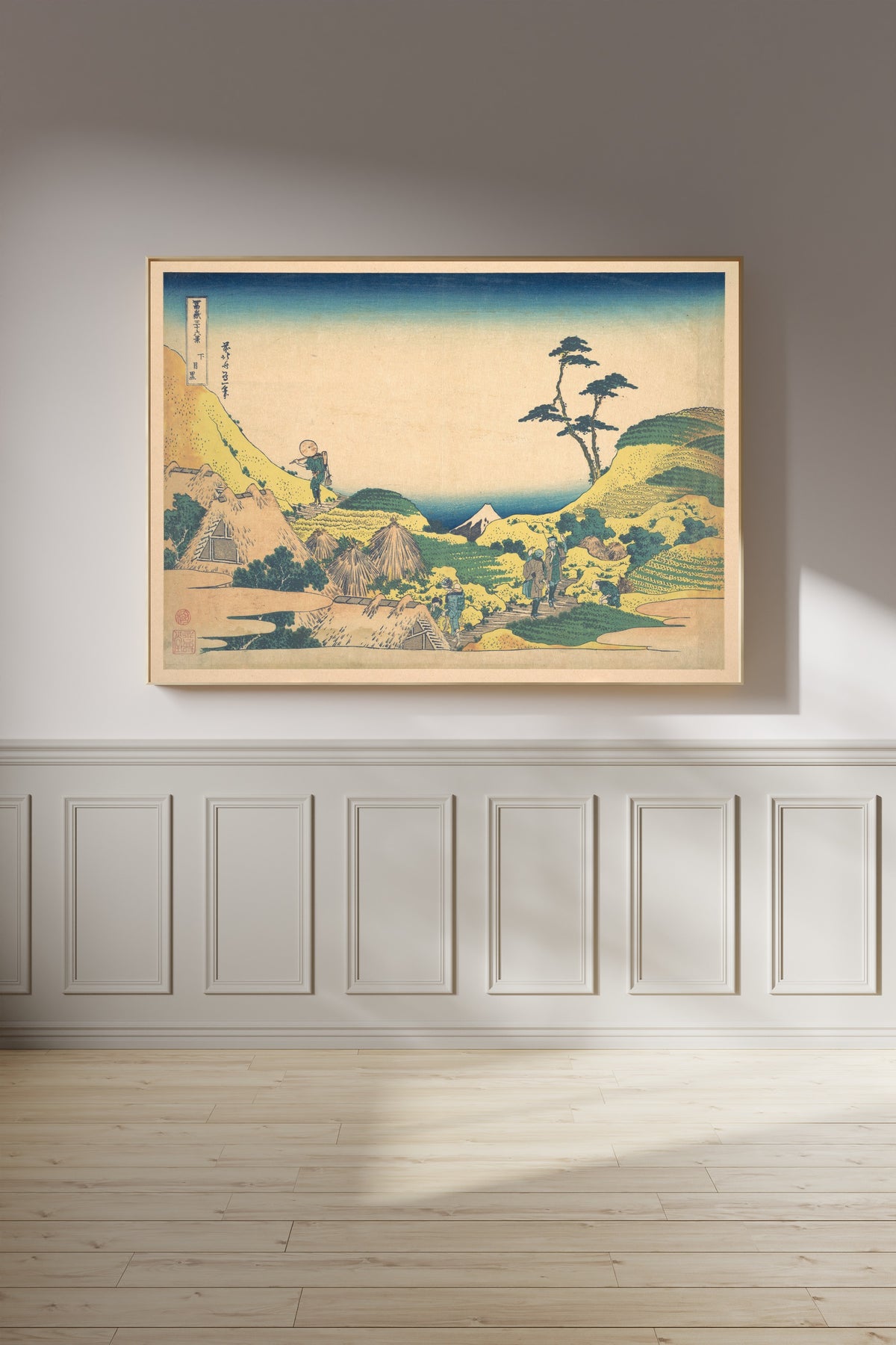 Framed art print of Thirty-six Views of Mount Fuji: Lower Meguro by Katsushika Hokusai, on a panelled wall in afternoon light